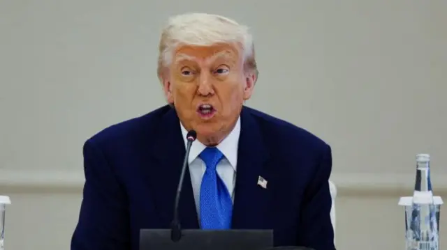 Trump speaking in at a white conference desk in the UAE