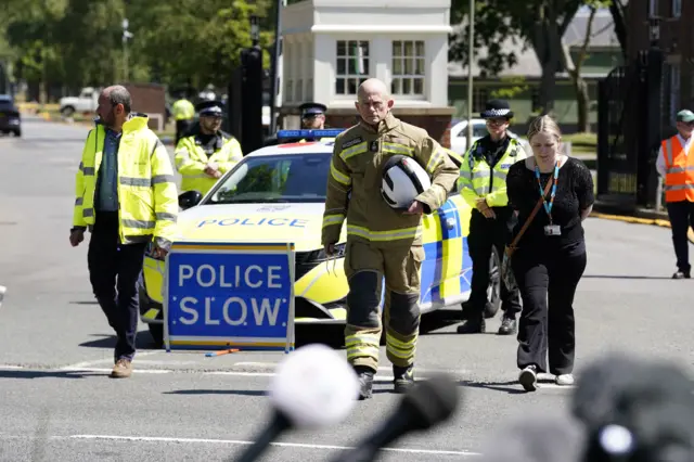 Fire chief arrives to give press update in front of a police van and other emergency services
