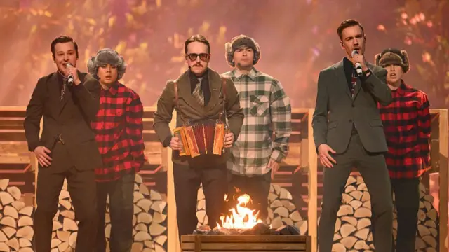 Sweden entrants KAJ perform on stage in suits with men in chequered shirts standing behind them