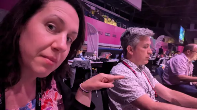 BBC reporter points next to another in the press room