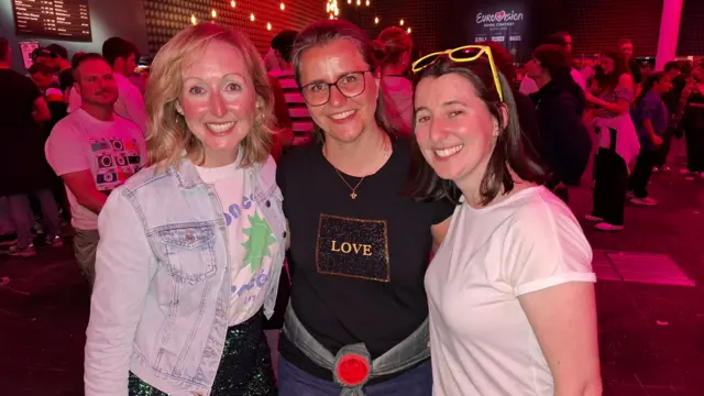 Hannah (L), her friend and Sinead (R) pose inside the Eurovision Village in Basel