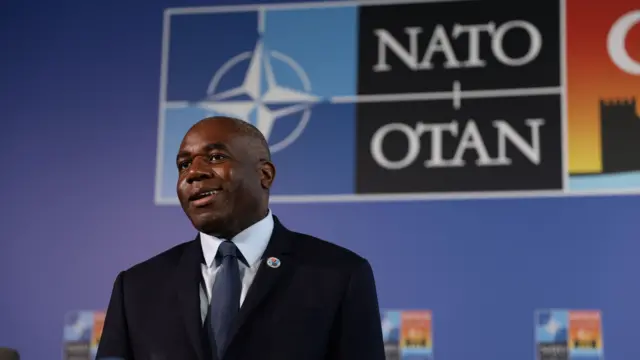 A headshot David Lammy against the backdrop of a Nato sign