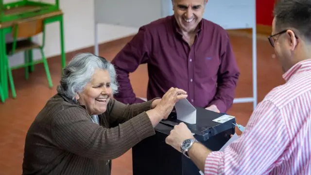 A voter with grey hair smilinglu casts her vote for the 2025 legislative elections at a polling station in Lisbon, Portugal