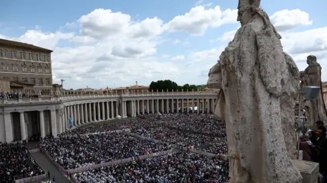 A overhead shot of St Peter's Square filled with people. On the right hand side is a statue