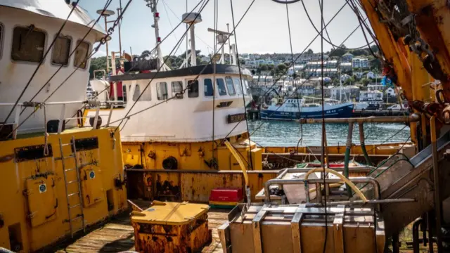 An image taken from on board a fishing trawler, another can be seen behind and the harbour behind that