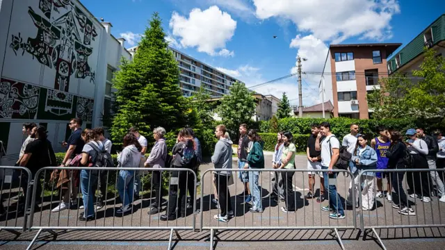 Students wait in line to vote at a polling station in Bucharest. A queue of young people, both women and men, waits in line behind a metal barrier outside a group of buildings
