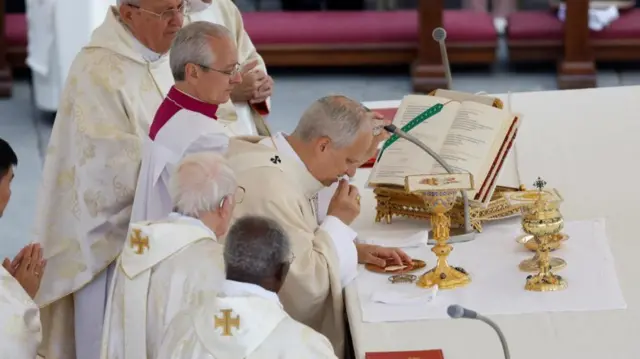 Pope Leo at the altar taking communion. Other men in religious clothing stand around