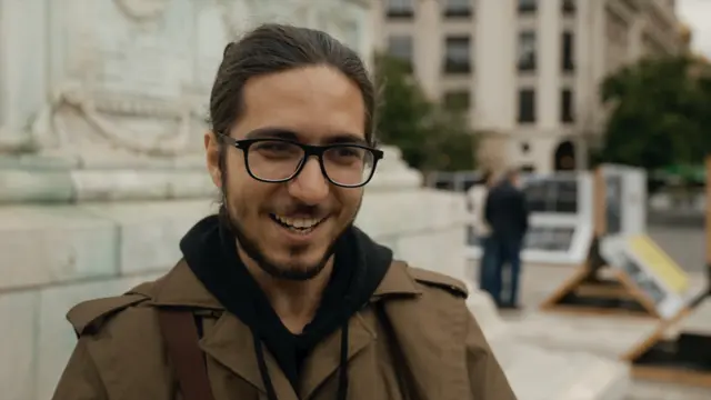 A man with long hair tied back, with a beard and glasses, smiles