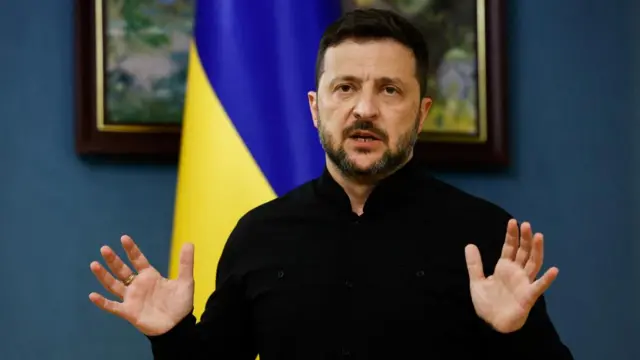 Ukrainian President Zelensky standing in front of a Ukrainian flag.
