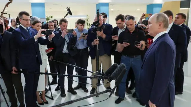 Putin stood in front of a large microphone with people stood around him.