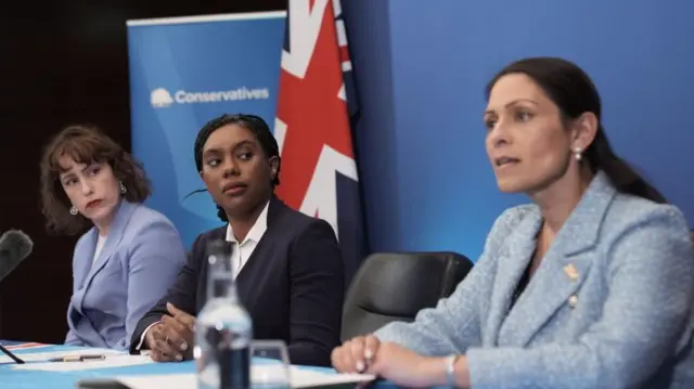 Atkins, Badenoch and Patel sit at a desk for a press conference