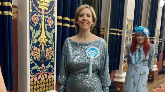 Andrea Jenkyns walks into the count with a smile on her face and wearing a Reform rosette