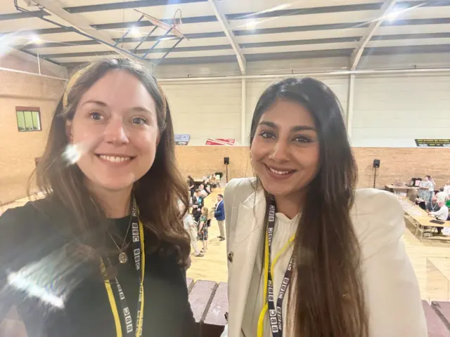 Kate and Shariqua smile at the camera as they take a selfie. Shariqua is wearing a cream blazer and Kate has a dark jumper on.