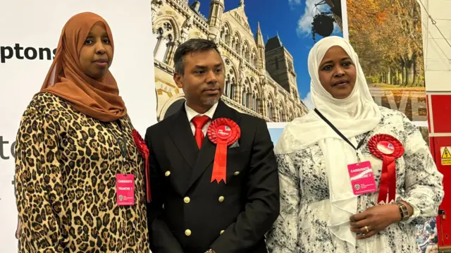 Muna Cali, Enam Haque and Fartun Ismail all on stage having been elected. They have red rosettes pinned to their chests and they look serious.