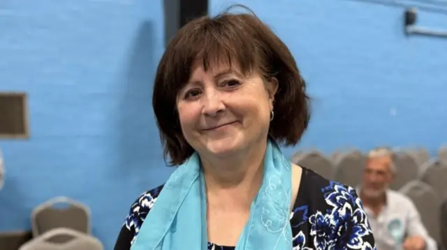A woman with dark hair and a pale blue scarf