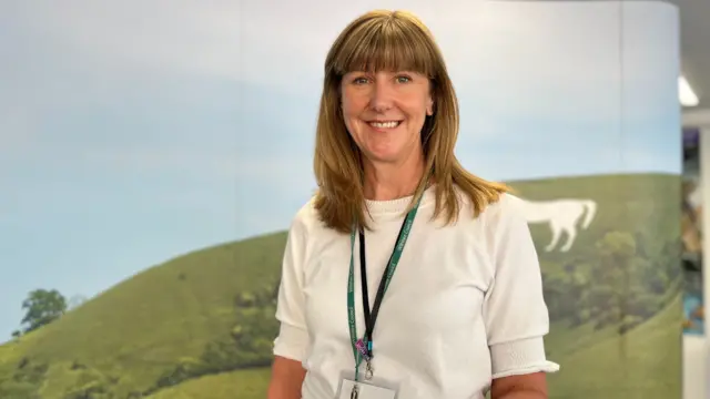 Emily Legg, she is wearing a white top and has a green lanyard on. She is smiling at the camera