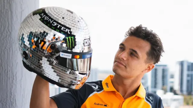 Lando Norris holds up his disco ball helmet