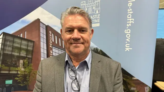 A man with grey hair, a pale blue shirt and a grey jacket