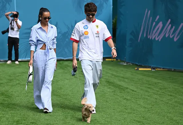 Alexandra Saint Mleux and Charles Leclerc walk into the paddock with their dog Leo