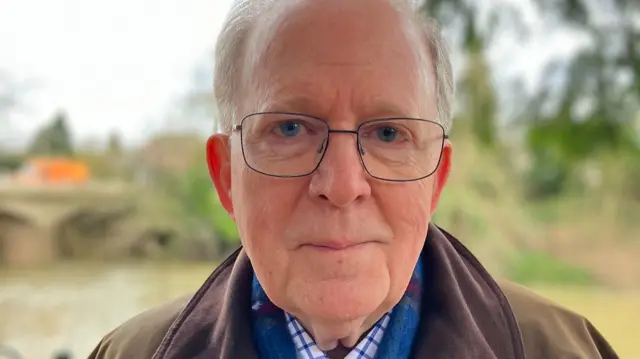 A man with grey hair and glasses looks at the camera.