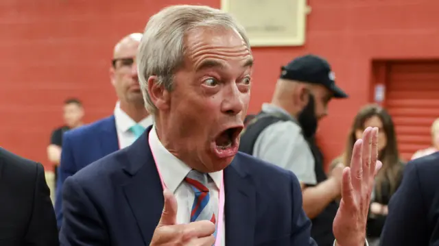 Nigel Farage holds up six fingers with a shocked expression on his face
