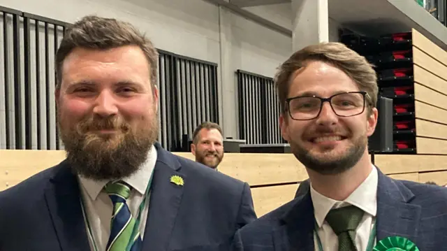 Ben Jameson and Ben Williams. Both are wearing navy suit jackets, white shirts and green ties. They are smiling together.