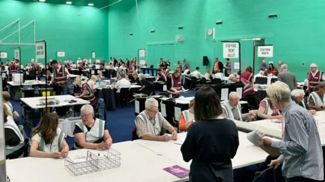 People sat at rows of tables with boxes and papers on them