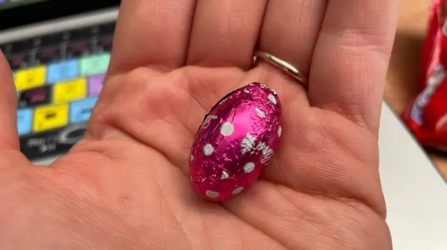 A mini chocolate egg wrapped in pink foil sitting in the palm of someone's hand.