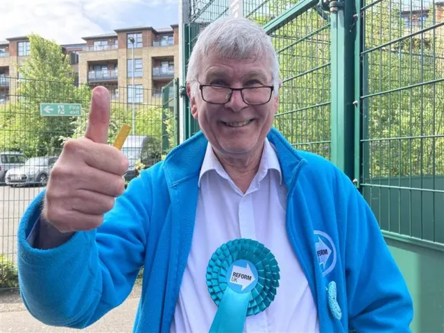 Reform councillor Bill Hopkins in a blue party fleece and rosette with his thumb held up.