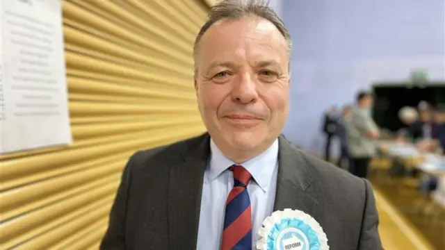 Aaron Banks is seen from his shoulders up. He is wearing a suit and is smiling at the camera.