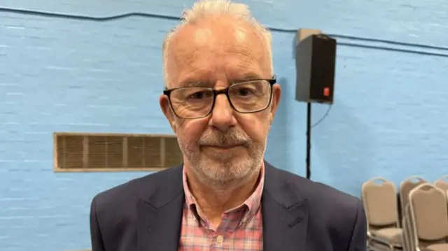 A man with grey hair and a beard with black glasses
