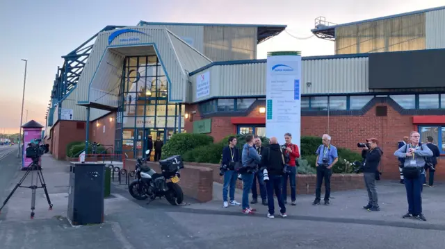People stand outside the centre where the votes are being counted - it's dawn and just light outside