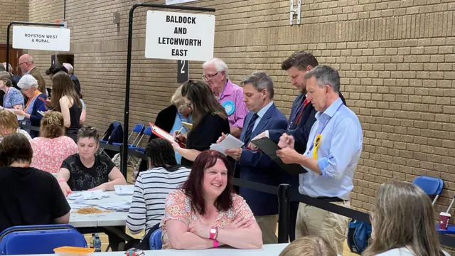 A group of people standing by tables, looking at notes and checking results.