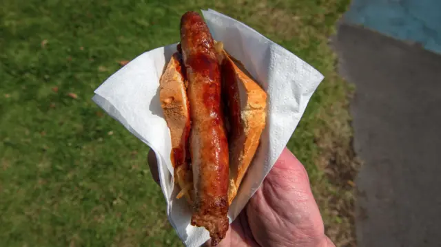 A sausage on bread held by someone with a piece of tissue