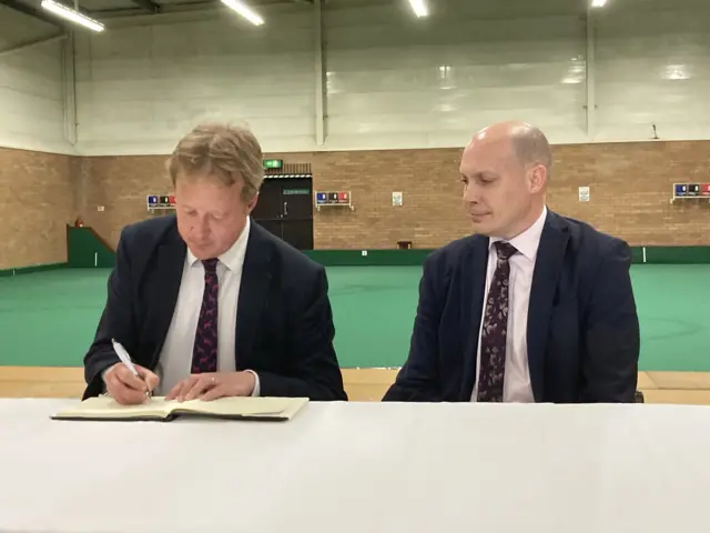 Paul Bristow signing his declaration of office at a table inside a sports hall.
