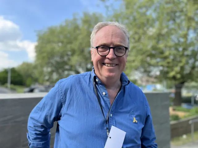Brian Mathew looks at the camera wearing a blue shirt