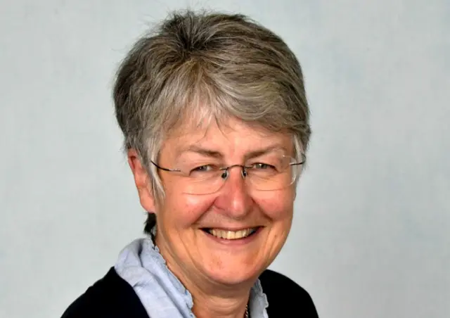 A smiling woman with greying hair and a pale blouse