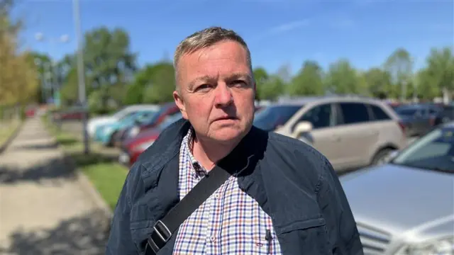 Gwilym Butler has short grey hair and is wearing a navy jacket with a red and blue shirt.