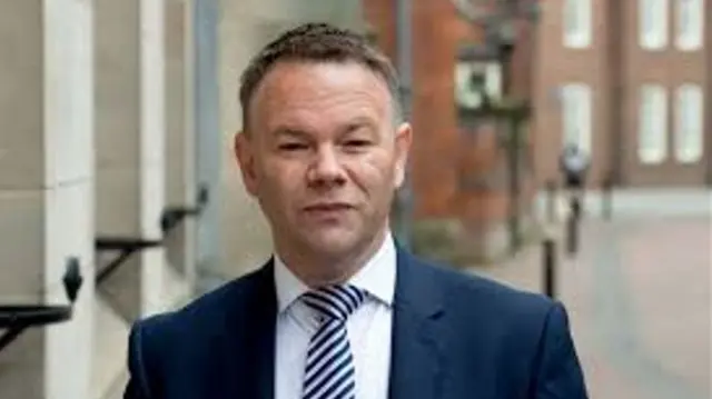 A man with short brown hair and a blue suit standing in a street