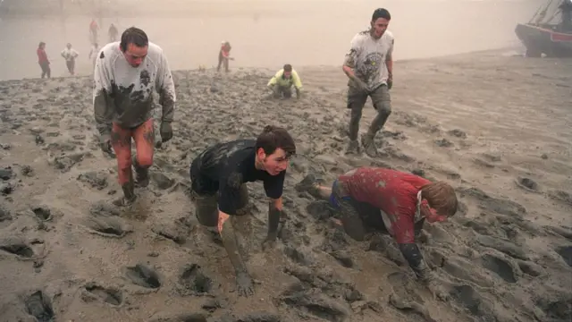 People making their way through thick mud along a muddy riverbank