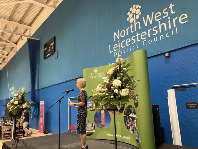 An image of a woman making an announcement with flowers either side