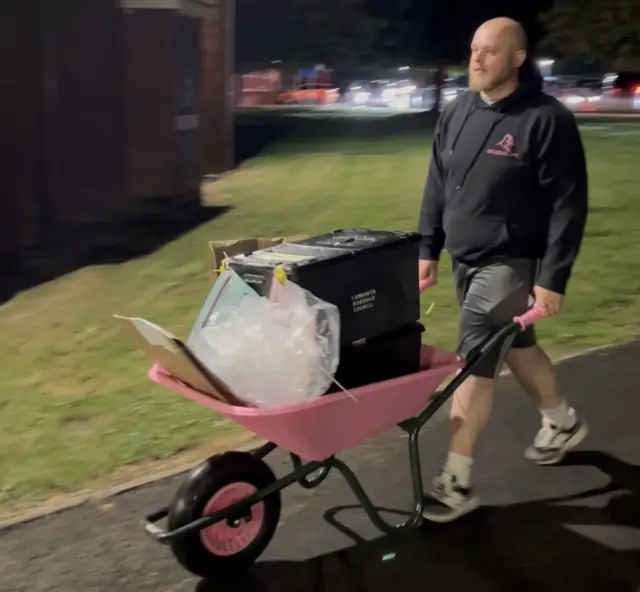 A man walks with black boxes containing votes in a pink wheelbarrow