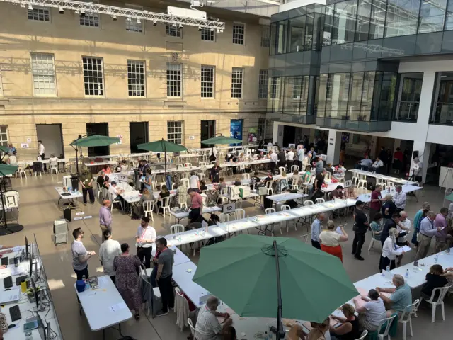 A view from above of people sat at trestle tables in rows for vote verification