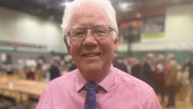 Christopher Wright looking at the camera while standing in a sports hall where an election count is taking place