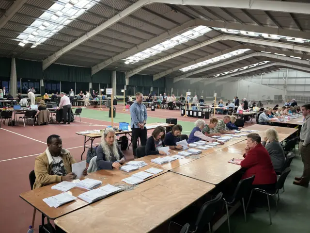 Many are sitting on long tables counting ballot papers in a large sports hall