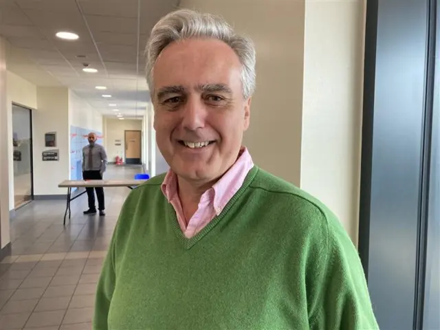 Tory MP Mark Garnier, smiling at the camera and wearing a pink collared shirt under a green v-neck jumper.