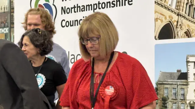 Wendy Randall wearing red on stage. She looks despondent.