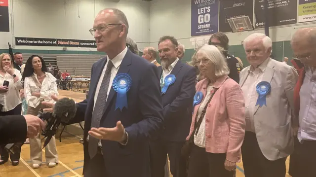 Richard Roberts standing in a room talking into a microphone, with a group of people behind him