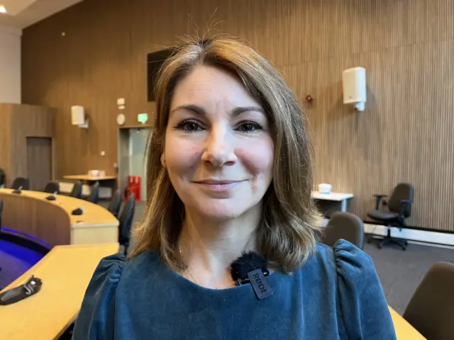 A woman standing in a council chamber smiling at the camera