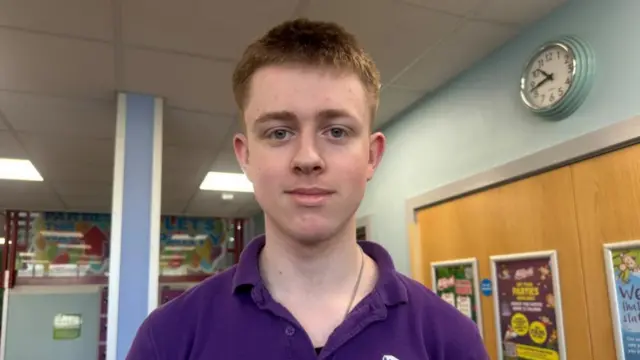 A man in a purple polo top standing in the reception area of a soft play centre. He has short brunette hair and is smiling.